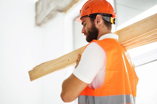 Builder man in hardhat carrying timber on building site, close up portrait