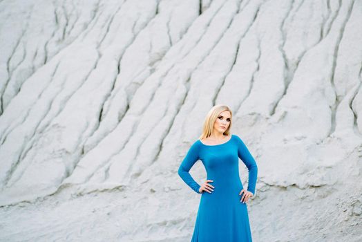 blonde girl in a blue dress with blue eyes in a granite quarry against the background of gravel