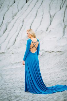 blonde girl in a blue dress with blue eyes in a granite quarry against the background of gravel