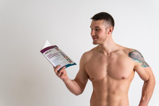 Bodybuilder reads the book on a white background isolated at the bottom of his head on his hands man muscular, athletic strong reader guy adult, sexy sport. Health vision tan