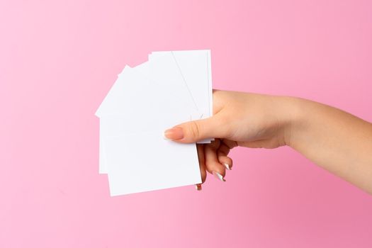 Woman hand showing blank business card on pink background. Close up.