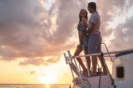 Beautiful loving couple looking at sunset from the yacht