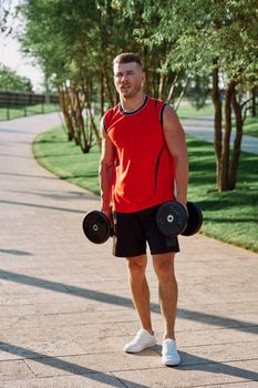 athletic man with dumbbells in his hands outdoors in the park. High quality photo