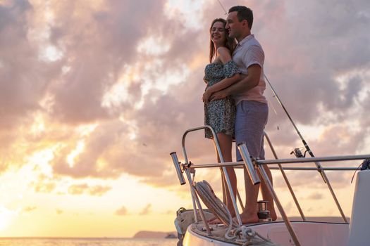 Beautiful loving couple looking at sunset from the yacht