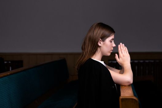 A Christian girl in white shirt is sitting and praying with humble heart in the church.