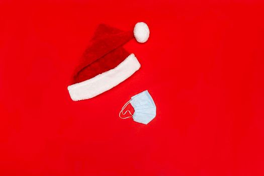 Flatlay with Santa red hat and blue facial protective medical mask on red background, no face, no poeple, Chrisstman conceptual photo, copy space.