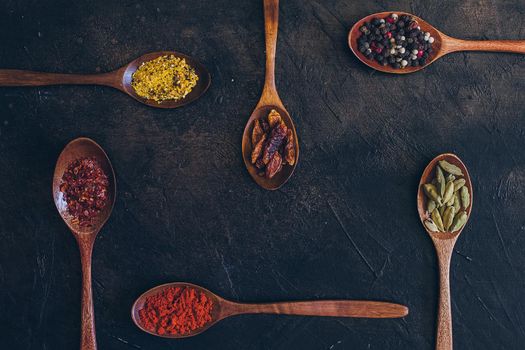 Various spices in wooden spoons on old black table