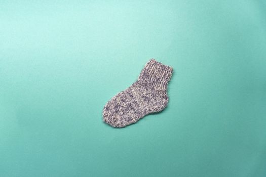 Knitted gray and white sock is on light green background. Flat lay of a handmade work.