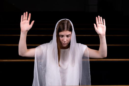 A young modest girl with a handkerchief on her head is sitting in church and praying. The concept of religion, prayer, worship.