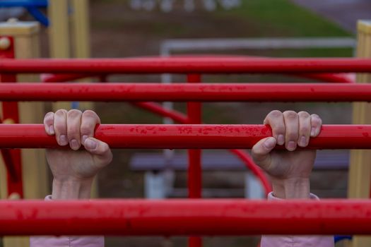 Girl hanging bar by 2 hands the outdoor exercise equipment. In public park, soft focus.