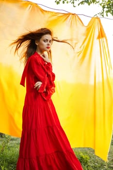 pretty woman in red dress yellow fabric on nature background. High quality photo