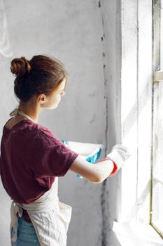 Woman in a white apron paints a window in a house interior renovation. High quality photo