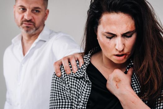 A woman beaten by her husband standing behind her and looking at her aggressively. Domestic violence.