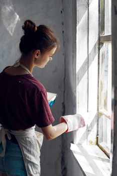 Woman in a white apron paints a window in a house interior renovation. High quality photo