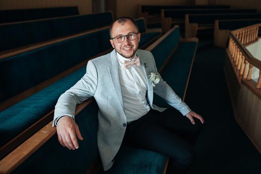 Wedding photo of emotions of a bearded groom with glasses in a gray jacket in the church building.