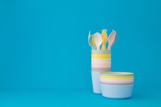 Colored reusable plates glasses spoons and forks on blue background copy space. Tableware for serving in pastel colors for a children's party