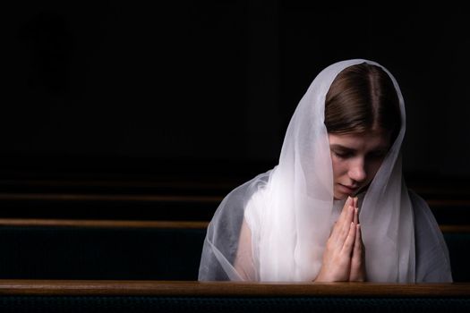 A young modest girl with a handkerchief on her head is sitting in church and praying. The concept of religion, prayer, worship.