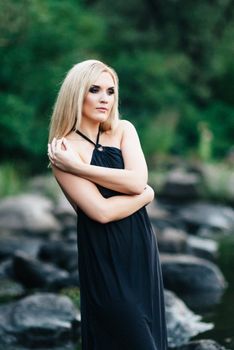 blonde girl in a black dress with blue eyes on the stone coast of the river