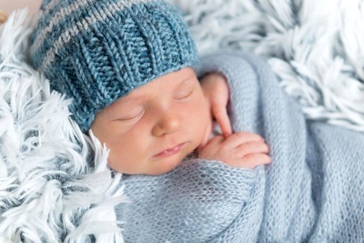 Sweet newborn infant boy is sleeping peacefully while snuggled in blue blankets. Newborn baby sleeping in small box with rabbit toy near him, top view