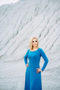 blonde girl in a blue dress with blue eyes in a granite quarry against the background of gravel