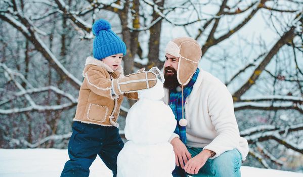 Winter, father and son play outdoo making snowman. Handmade funny snow man. Christmas family holidays with daddy