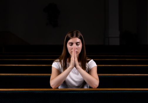 A Christian girl in white shirt is sitting and praying with humble heart in the church.