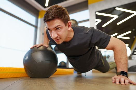 Fit young man exercising with fitness ball in a gym, close up