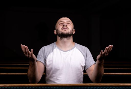 A Christian man in white shirt is sitting with his hands up and praying with humble heart in the church.