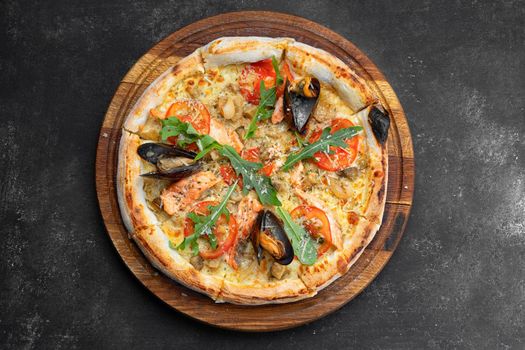 Pizza with seafood mussels shrimp salmon scallop on a wooden board, on a dark background