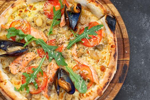 Pizza with seafood mussels shrimp salmon scallop on a wooden board, on a dark background