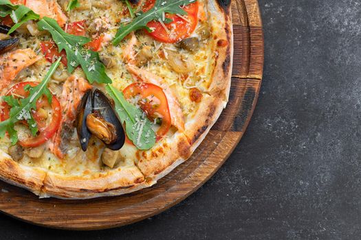 Pizza with seafood mussels shrimp salmon scallop on a wooden board, on a dark background