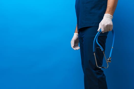 Unrecognizable male doctor holding stethoscope against blue background, close up