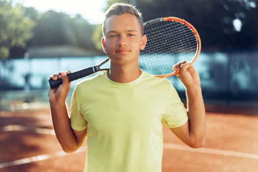 Young man teenager with tennis racket standing near net on clay tennis court