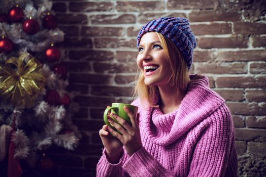 Winter hot drinks. Portrait of a young beautiful smiling drink hot tea at home. Smiling woman decorating Christmas tree at home