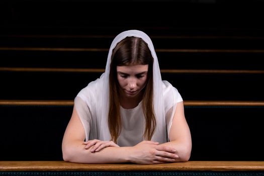 A young modest girl with a handkerchief on her head is sitting in church and praying. The concept of religion, prayer, worship.