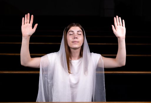 A young modest girl with a handkerchief on her head is sitting in church and praying. The concept of religion, prayer, worship.