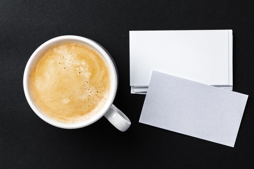 Top view of cup with espresso and white business card template on black table