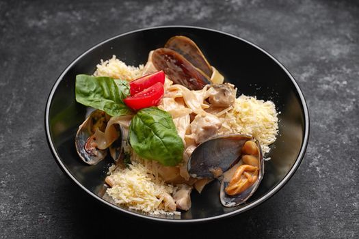 Pasta with seafood, mussels, scallop, rapana and cheese, on a black plate