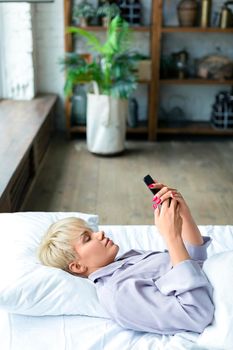 Vertical photo. woman lies in bed with cell phone. She woke up and was checking social media posts. Modern technology concept.