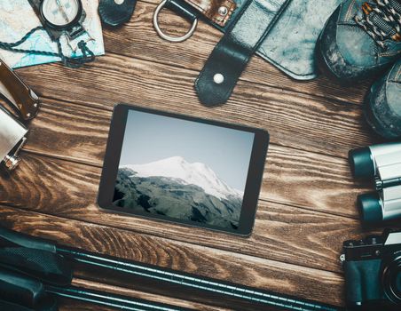 Equipment for travel and hiking around tablet with Elbrus picture on a wooden background, concept of wanderlust.