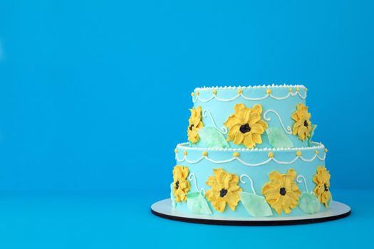 Two-tiered cake for a little girl princess with yellow flowers on blue background like a cartoon Beautiful sunflower decorated cake