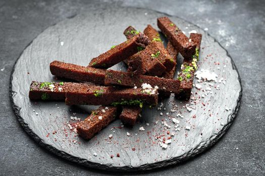 Black bread toast for beer with garlic salt and herbs on a black background