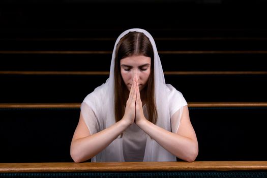 A young modest girl with a handkerchief on her head is sitting in church and praying. The concept of religion, prayer, worship.