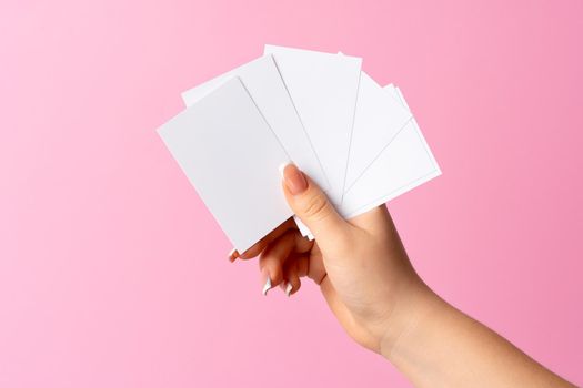 Woman hand showing blank business card on pink background. Close up.