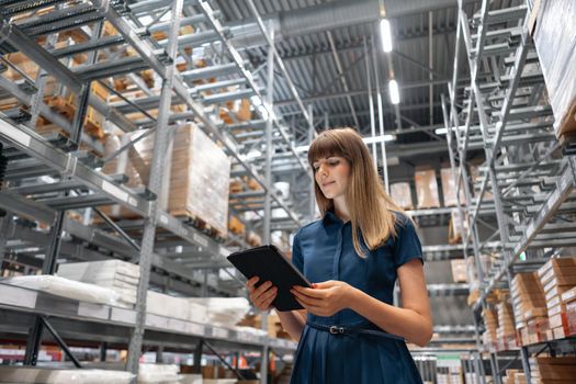 Wholesale warehouse. Beautiful young woman worker of store in shopping center. Girl looking for goods with a tablet is checking inventory levels in a warehouse. Logistics concept.