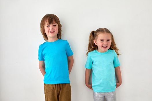 Adorable happy brother and sister in blue t shirts smiling and looking at camera while standing against gray wall