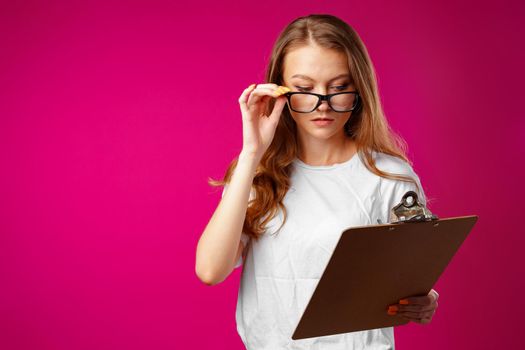 Young beautiful smiling woman standing and holding clipboard against pink background