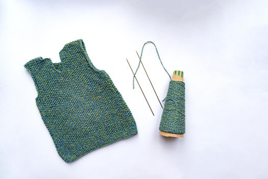 Waistcoat, thread, needles are on white background, view from the top. Knitting concept.