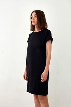 Adult female model in casual basic black midi dress standing against white background and looking away