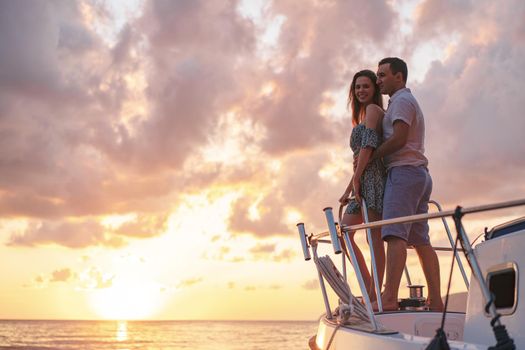 Beautiful loving couple looking at sunset from the yacht